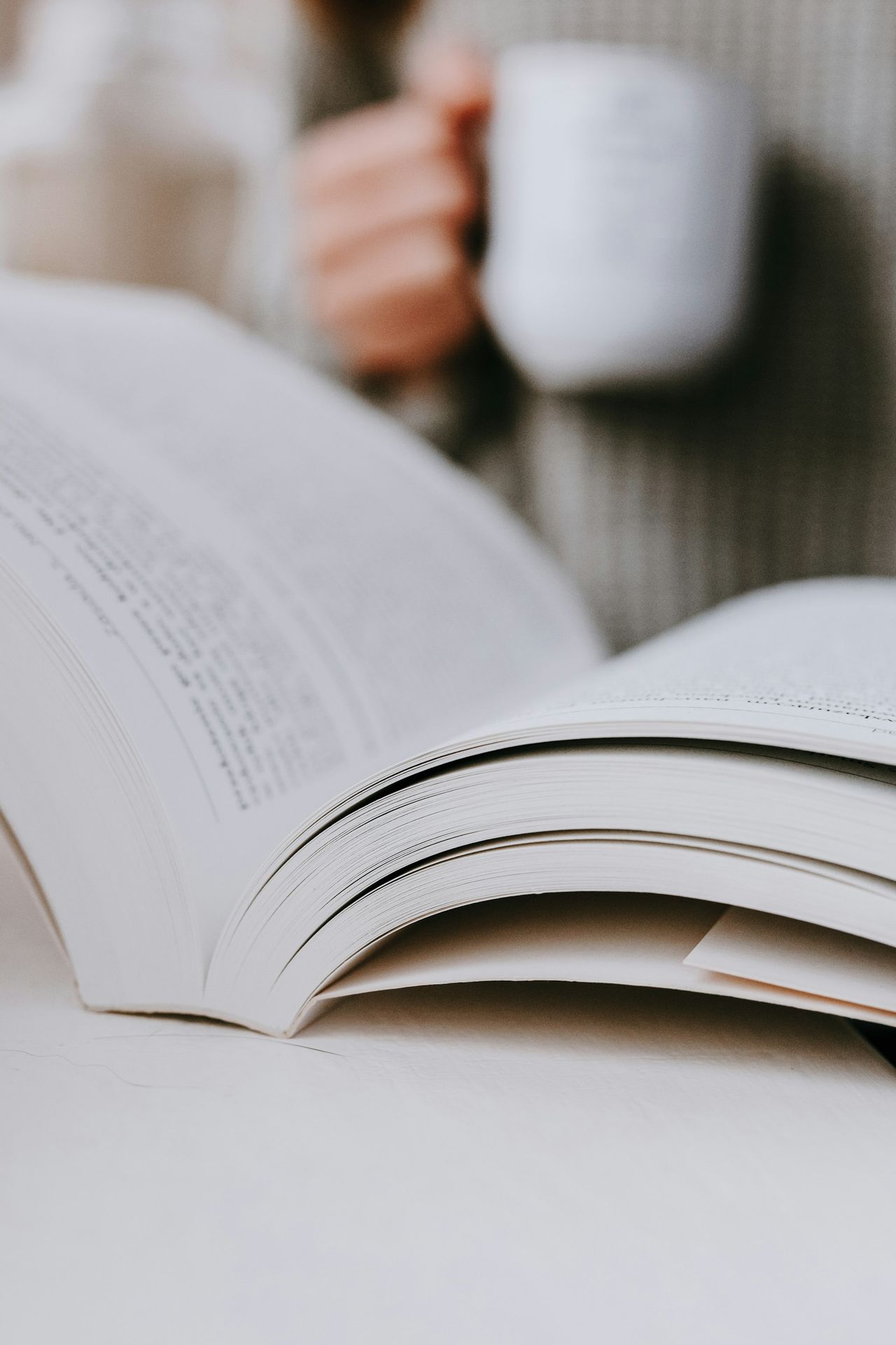 A person holding a cup of coffee while reading a book